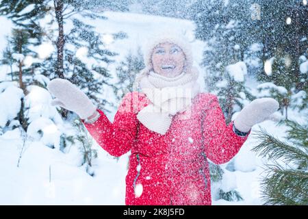 Frau mittleren Alters lächelt und spielt mit Schnee im Wald Stockfoto