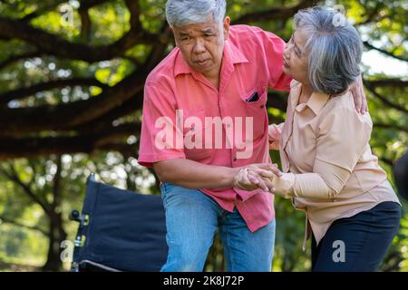 Ein älterer Mann aus Asien fiel auf den Boden im Park, nachdem er gestolpert und vor Schmerzen geweint hatte, und seine Frau kam, um zu helfen. Konzept der alten älteren Insu Stockfoto