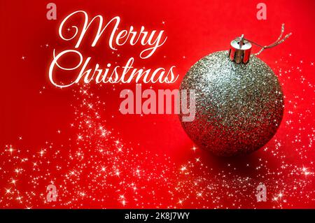 Frohe Weihnachtswünsche mit silberner Kugel und leuchtenden Sternen auf rotem Hintergrund. Weihnachtsfeier Konzept. Stockfoto