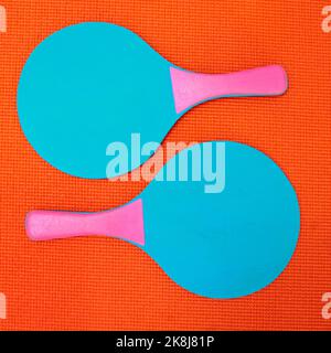 Wer will mich mitnehmen. High-Angle-Aufnahme von zwei blauen Tischtennisschlägern, die auf einem orangefarbenen Hintergrund in einem Studio platziert sind. Stockfoto