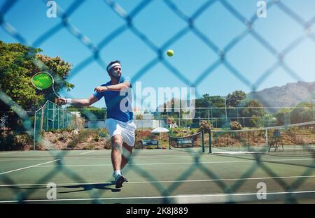 Mich selbst an meine Grenzen zu schieben. Ganzkörperaufnahme eines hübschen jungen Sportlers, der tagsüber alleine auf einem Platz Tennis spielt. Stockfoto