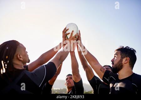 Die Macht liegt in unseren Händen. Eine ansehnliche Gruppe von Sportlern hält einen Rugby-Ball zusammen, bevor sie Rugby spielen. Stockfoto