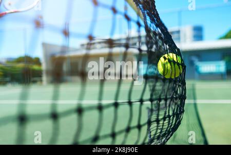 Ein Tennisball, der tagsüber ein Tennisnetz auf dem Platz trifft. Stockfoto