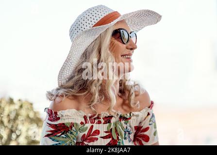 Sommer war schon immer ihre Art von Stimmung. Eine attraktive ältere Frau lächelt, während sie an einem Sommertag im Freien sitzt. Stockfoto
