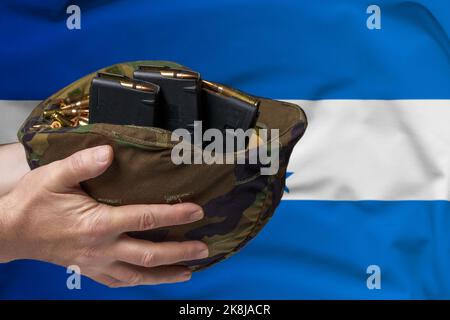 Ein Militärhelm mit Patronen und Zeitschriften für ein Gewehr in den Händen eines Mannes vor dem Hintergrund der Flagge von Honduras. Das Konzept von Stockfoto