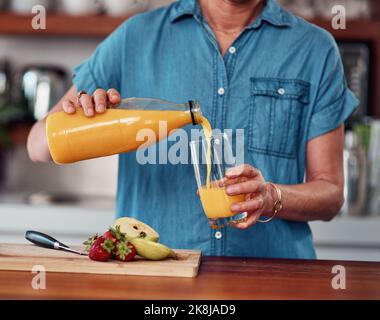 Das beste Frühstücksgetränk. Eine nicht erkennbare ältere Frau goss sich ein Glas Orangensaft, während sie das Frühstück in der Küche zubereitete. Stockfoto