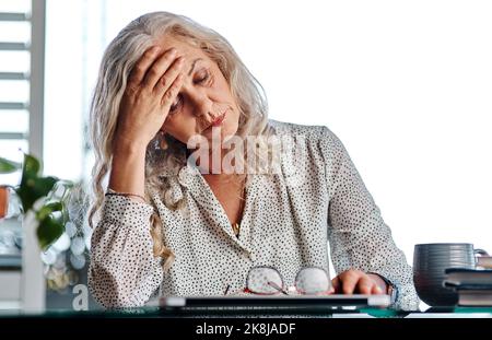Ich bin so erschöpft... eine attraktive Geschäftsfrau, die bei der Arbeit von zu Hause aus Kopfschmerzen hat. Stockfoto