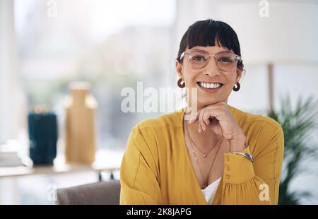 Ihr Lächeln ist Teil Ihrer Persönlichkeit. Das verkürzte Porträt einer attraktiven jungen Geschäftsfrau, die allein in ihrem Büro mit der Hand auf dem Kinn sitzt. Stockfoto