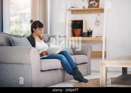 Der Realität durch einen Roman entkommen. In voller Länge eine attraktive junge Frau, die allein in ihrem Wohnzimmer sitzt und ein Buch liest. Stockfoto