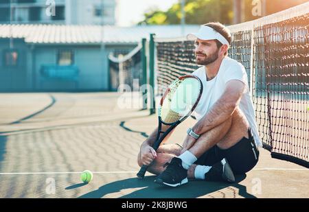 Es war mein Traum, ein Tennis-Superstar zu werden. Ein sportlicher junger Mann, der auf einem Tennisplatz sitzt. Stockfoto