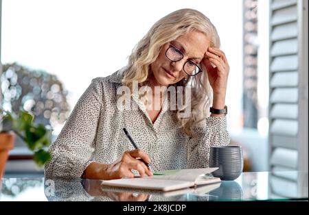 Das bereitet mir Kopfschmerzen. Eine attraktive Geschäftsfrau, die bei der Arbeit von zu Hause aus Kopfschmerzen hat. Stockfoto