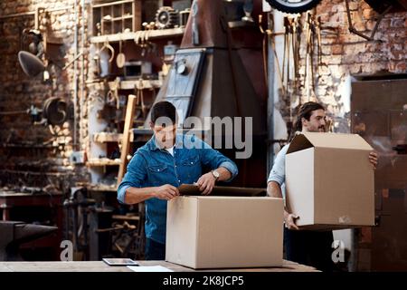 Die Dinge werden einfacher, wenn wir zusammenarbeiten. Zwei junge Geschäftsleute tragen Kisten, während sie Bestellungen und Lieferungen in ihrer Werkstatt sortieren. Stockfoto