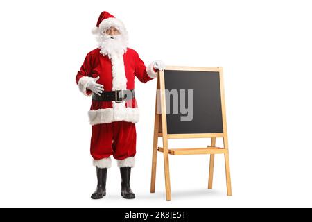 Der weihnachtsmann steht neben einer kleinen Schultafel mit einem Holzrahmen und steht isoliert auf weißem Hintergrund Stockfoto