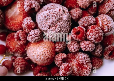 Rote gefrorene Beeren bedeckt mit Frost auf weißem Teller. Himbeeren, Erdbeeren, rote Johannisbeeren. Erhaltung der Sommervitamine für den Winter Stockfoto