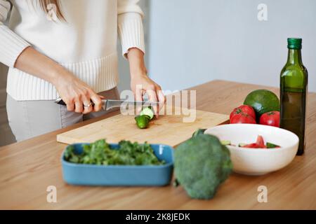 Nahaufnahme der Hände der Frau, die veganen Salat mit frischem Gemüse zubereitet. Modellschneiden mit Messer-Avocados, Brokkoli, Grünkochsalat, Gurken und Tomaten in Stockfoto