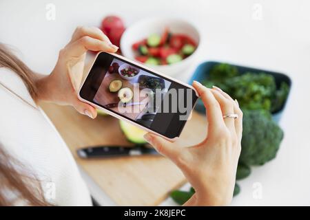 Die Hände des Food-Bloggers fotografieren mit dem Smartphone und mischen frischen grünen Salat auf weißem Hintergrund, um in den sozialen Medien zu teilen Stockfoto