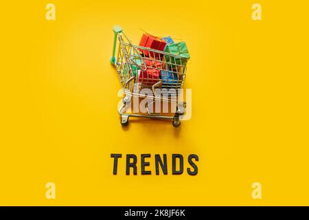ECommerce Retail Shopping Trends Konzept. Word Trends und Mini-Warenkorb mit Box auf gelbem Hintergrund. Stockfoto