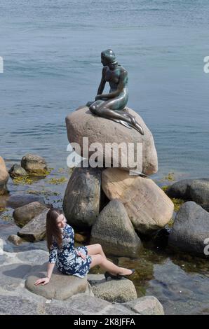 Mädchen posiert für ein Foto vor der kleinen Meerjungfrau-Statue am Wasser, Kopenhagen, Dänemark Stockfoto