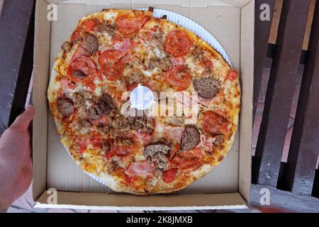 Nahaufnahme einer Schachtel mit Thin Crust Pizza, garniert mit Schinkenpepperoni und Würstchen Stockfoto