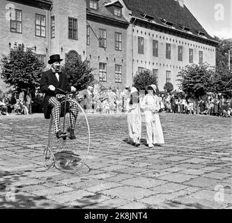 Bygdøy 19570825 Parade von alten Fahrrädern im Volksmuseum. Mann mit Zahnseide-Hut und moderner Kleidung auf dem alten Fahrrad des velociped/Tiltpetter-Typs. Im Hintergrund zwei Frauen, modisch gekleidet mit langen Kleidern und Küssen. Foto: Jan Nordby / NTB / NTB Stockfoto