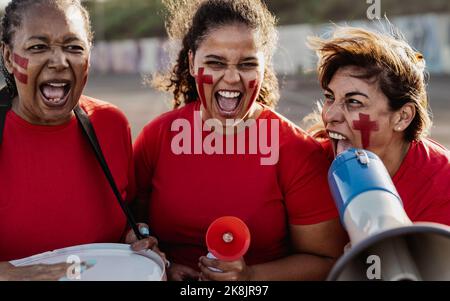 Fußballfans jubelten beim Fußballspiel im Stadion - Frauen mit gemaltem Gesicht und Megaphon ermutigen ihr Team Stockfoto