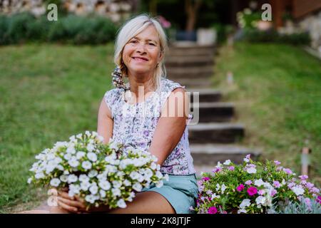 Ältere Frau im Garten zu Hause mit ihren Blumen. Stockfoto