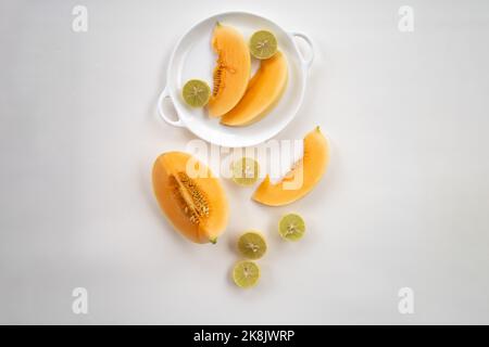Eine Draufsicht auf süße, frische Melonen- und Zitronenscheiben auf einem Teller, der auf weißem Hintergrund isoliert ist Stockfoto