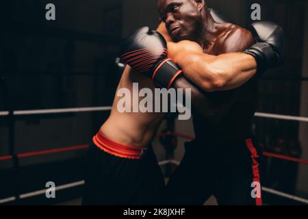 Zwei männliche Kämpfer kämpfen mit Handschuhen in einem Boxring. Zwei sportliche junge Männer, die in einem Fitnessstudio einen Boxkampf führen. Stockfoto