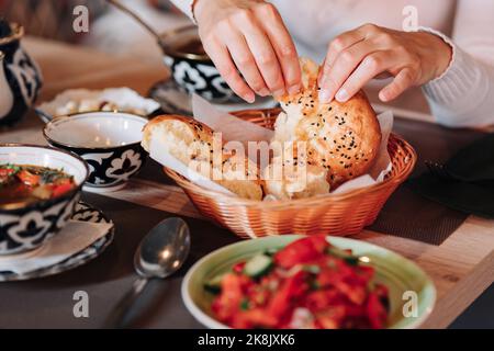 Weibliche Hände halten selbstgebackenes, natürliches frisches Brot mit einer goldenen Kruste. Traditionelles asiatisches usbekisches Brot. Stockfoto