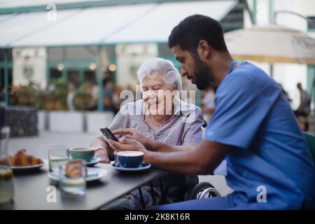 Pfleger, der Kaffee mit seinem Kunden hat und sie mit dem Smartphone im Café im Freien lernt. Stockfoto