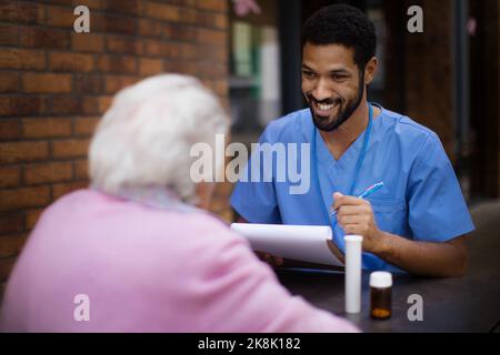 Pfleger erklärt Einnahme von Pillen zu älteren Frau. Stockfoto