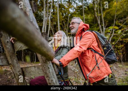 Glückliches Seniorenpaar, das auf der Jagd auf hohen Sitz im Herbstwald klettert. Stockfoto