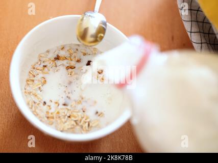 Nahaufnahme einer Schwangeren in der Schürze, die Milch in eine Schüssel mit Hafer gießt. Stockfoto