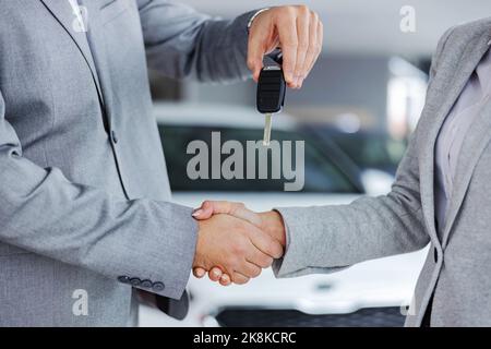 Nahaufnahme eines Autoverkäufers, der die Hände mit dem Kunden schüttelt und ihr die Autoschlüssel überreicht, während er im Autosalon steht. Stockfoto