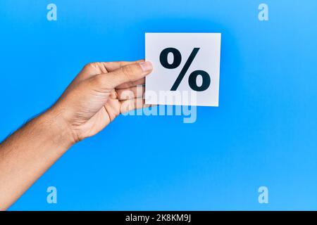 Hand eines kaukasischen Mannes, der Papier mit einer Prozentmarke auf einem isolierten blauen Hintergrund hält Stockfoto