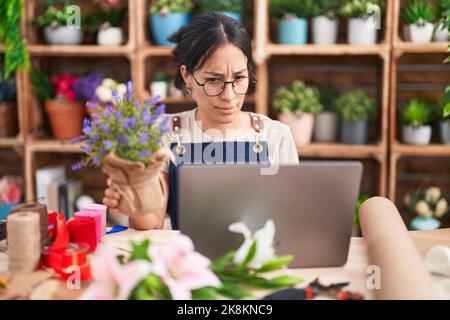 Junge hispanische Frau, die im Floristen-Shop arbeitet, macht Videoanruf skeptisch und nervös, runzelte wegen des Problems die Stirn. Negative Person. Stockfoto