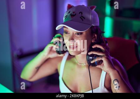 Junge schöne hispanische Frau streamer hält Kopfhörer im Spielzimmer Stockfoto