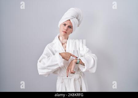 Blonde kaukasische Frau trägt einen Bademantel in Eile und zeigt auf Zeit, Ungeduld, aufgeregt und wütend auf die Verzögerung der Frist Stockfoto