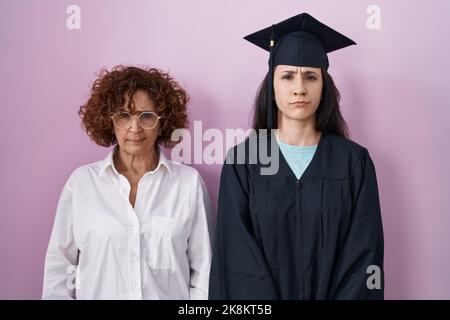 Hispanische Mutter und Tochter tragen Abschlusskappe und Zeremonie Robe skeptisch und nervös, Stirnrunzeln aufgeregt wegen des Problems. Negative Person. Stockfoto