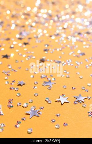 Schimmernde silberne Sterne und Kristalle Konfetti auf gelbem Hintergrund. Selektiver Fokus. Leuchtende Textur. Stockfoto