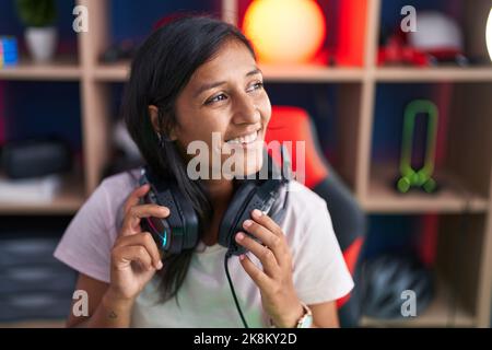 Junge schöne hispanische Frau streamer lächelnd zuversichtlich hält Kopfhörer im Spielsalon Stockfoto