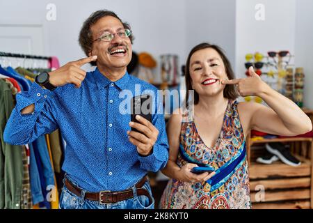 Interracial Paar mittleren Alters im Einzelhandel mit Smartphone lächelnd fröhlich zeigen und zeigen mit Fingern Zähne und Mund. Zahngesundheit concep Stockfoto