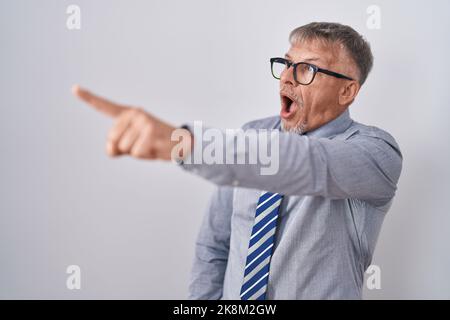 Hispanischer Geschäftsmann mit grauen Haaren, Brille mit dem Finger, überrascht, offener Mund, verblüffter Ausdruck, etwas auf der Vorderseite Stockfoto