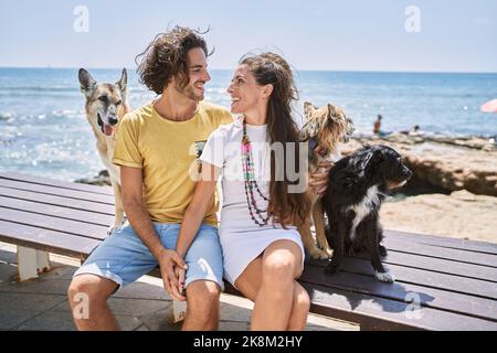 Mann und Frau Paar lächeln selbstbewusst und umarmen sich am Meer mit Hunden Stockfoto