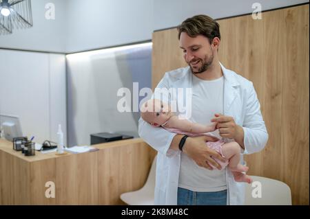 Fröhlicher junger Kinderarzt, der die Reflexe eines Neugeborenen überprüft Stockfoto