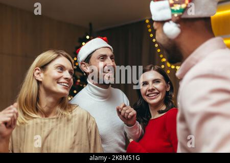 Neujahrsparty verschiedener verwitweter Freunde, Männer und Frauen tanzen aus nächster Nähe, lächeln fröhlich und umarmen das neue Jahr im Wohnzimmer in der Nähe des Weihnachtsbaums. Stockfoto