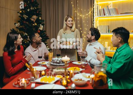 Festliches Weihnachts-Neujahrsessen, verschiedene Freunde feiern das neue Jahr gemeinsam zu Hause, essen zu Abend und trinken Alkohol am Festtisch. Stockfoto