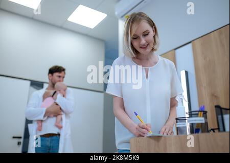 Mutter füllt vor der primären Konsultation den Papierkram für ihr Kind aus Stockfoto