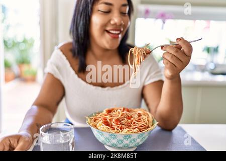 Hispanische Brünette Frau essen Spaghetti in der Küche Stockfoto