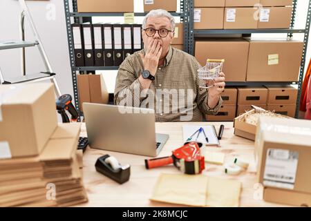 Leitender kaukasischer Mann, der bei E-Commerce-Geschäften in Kleinunternehmen arbeitet, hält einen Einkaufswagen, der den Mund mit der Hand bedeckt, schockiert und vor Fehlern fürchtet Stockfoto